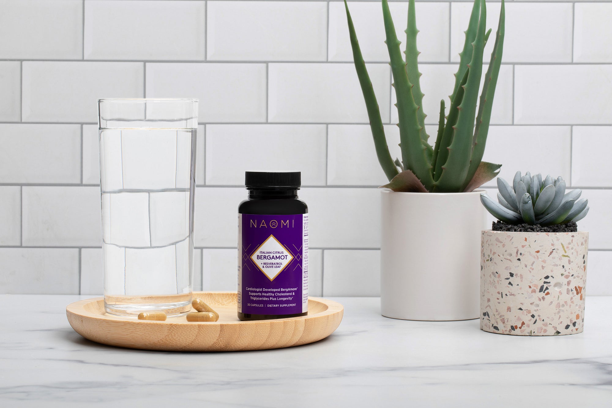 Nadmi supplement bottle on a wooden tray with plants and a glass of water in the background.