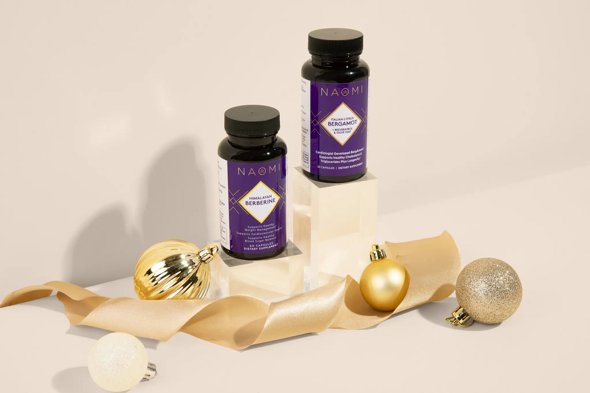 Two purple bottles with gold ribbons and Christmas ornaments on a beige background