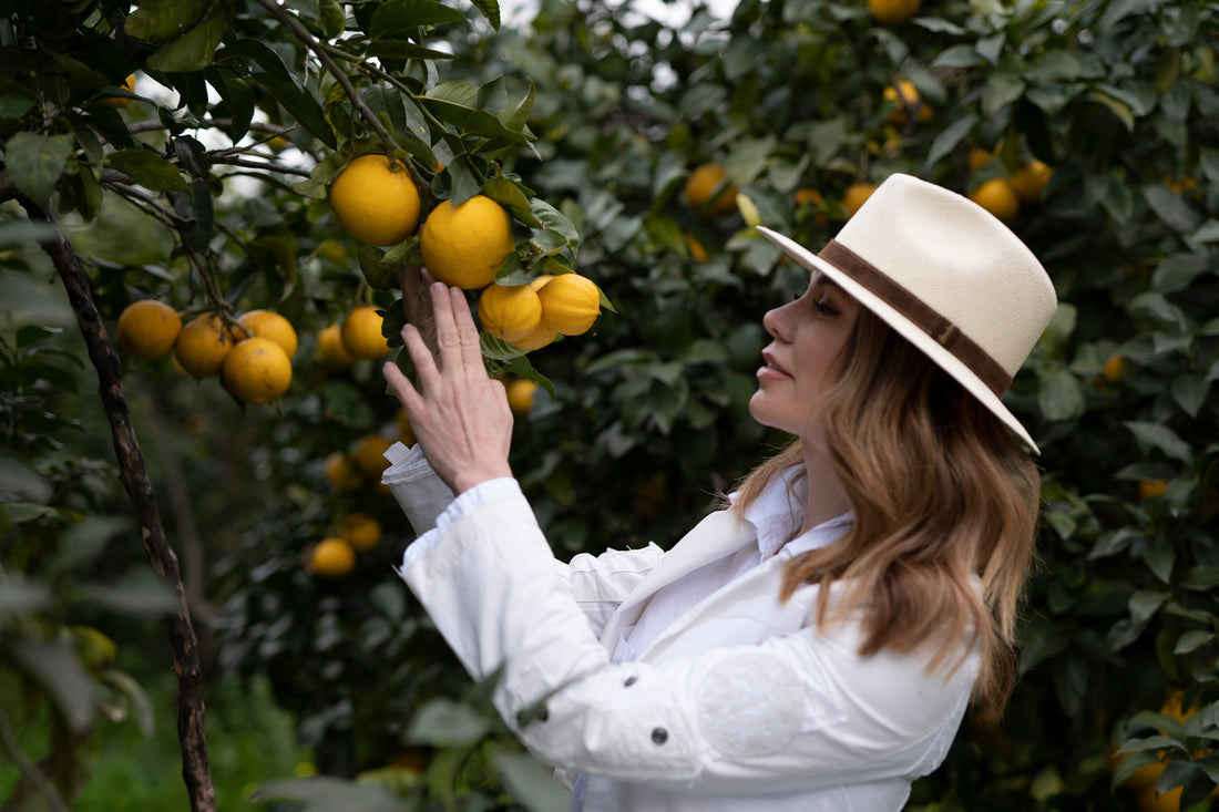 Naomi Whittel in a white coat and hat inspecting bergamots on a tree in an orchard.