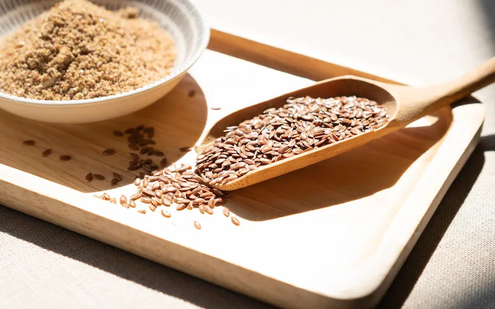 Wooden scoop filled with seeds on a wooden tray with a bowl of seeds beside it.