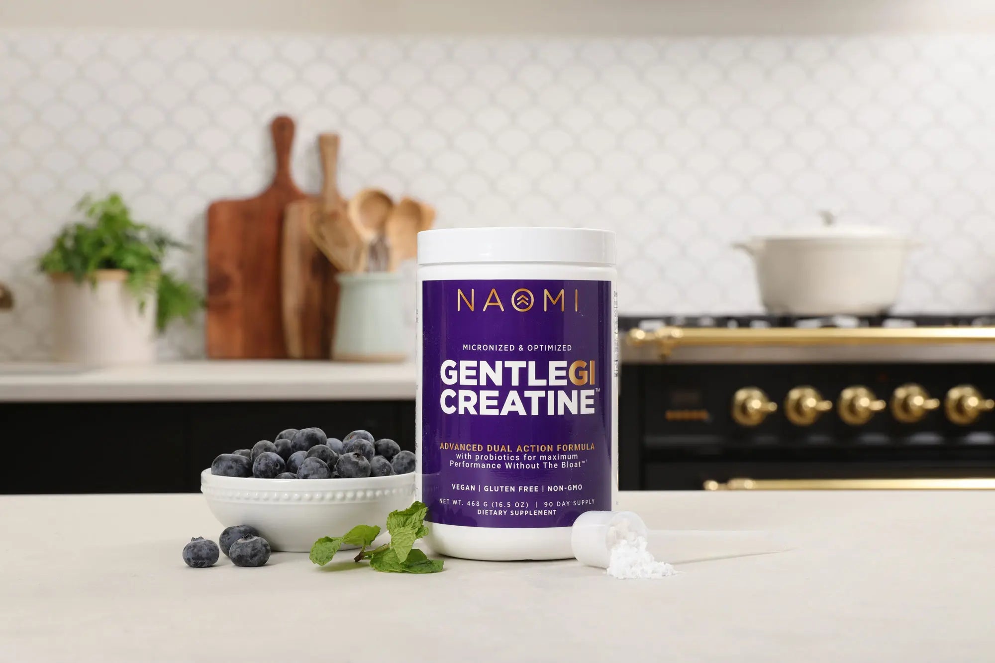 Container of Naomi Gentle GI Creatine on a kitchen counter with berries and a plant in the background.