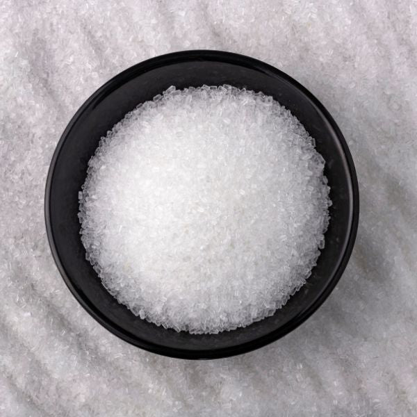 Black bowl filled with white granulated sugar on a gray surface