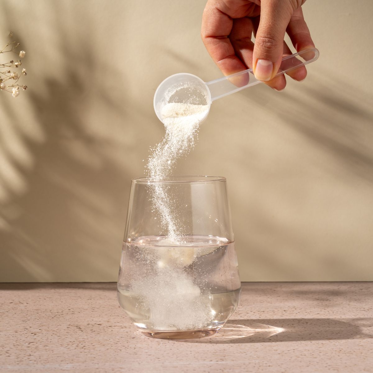 Person pouring powder from a scoop into a glass of water on a neutral background