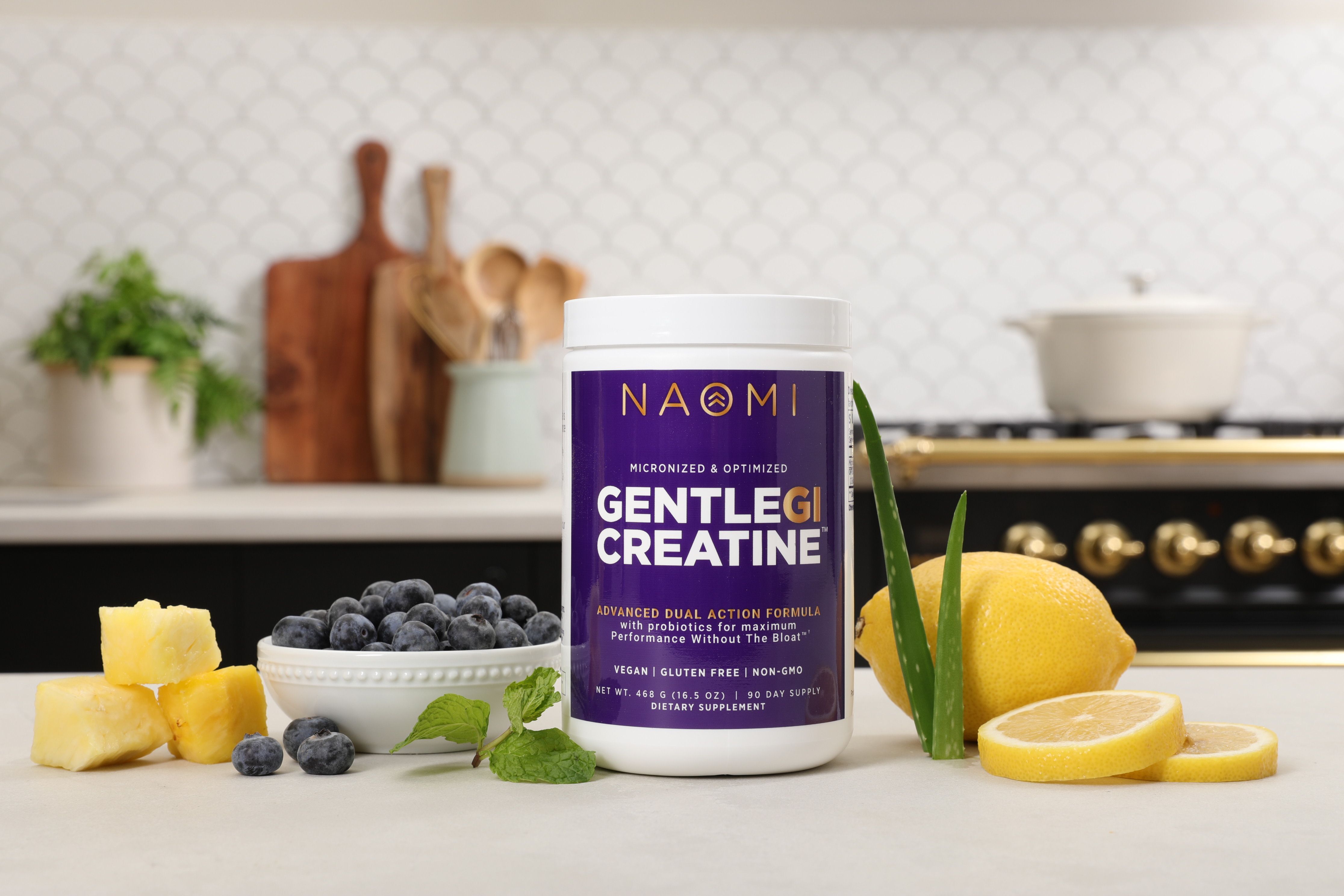 Container of Naomi Gentle Creatine on a kitchen counter with fruits and vegetables.