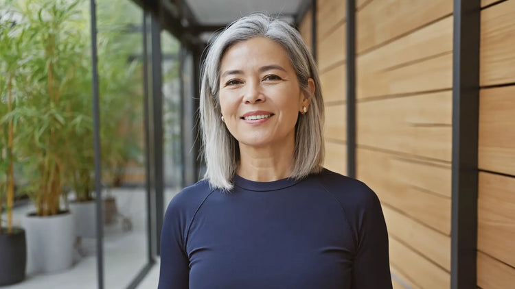 Woman with gray hair wearing a navy blue shirt standing in front of a wooden wall.