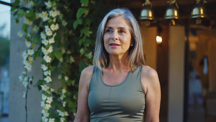 Woman in a green tank top standing outdoors with plants and lights in the background