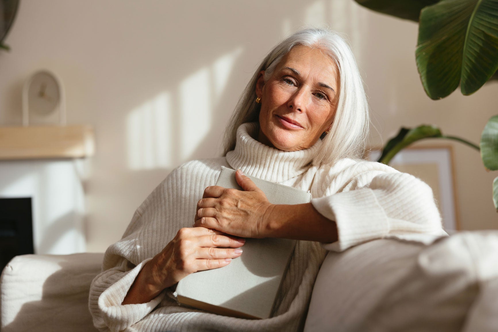 Woman sitting on a couch holding a cup in a cozy living room.