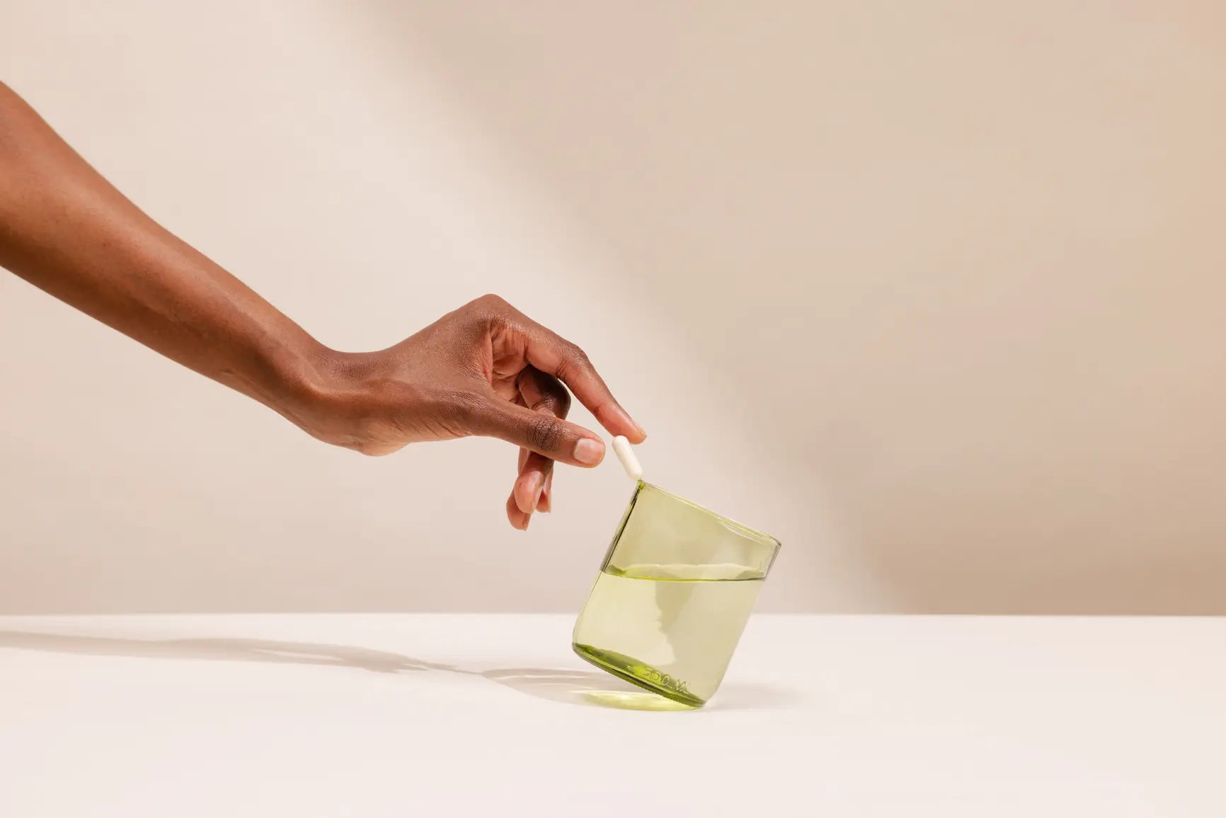 Hand holding a green glass vase against a beige background