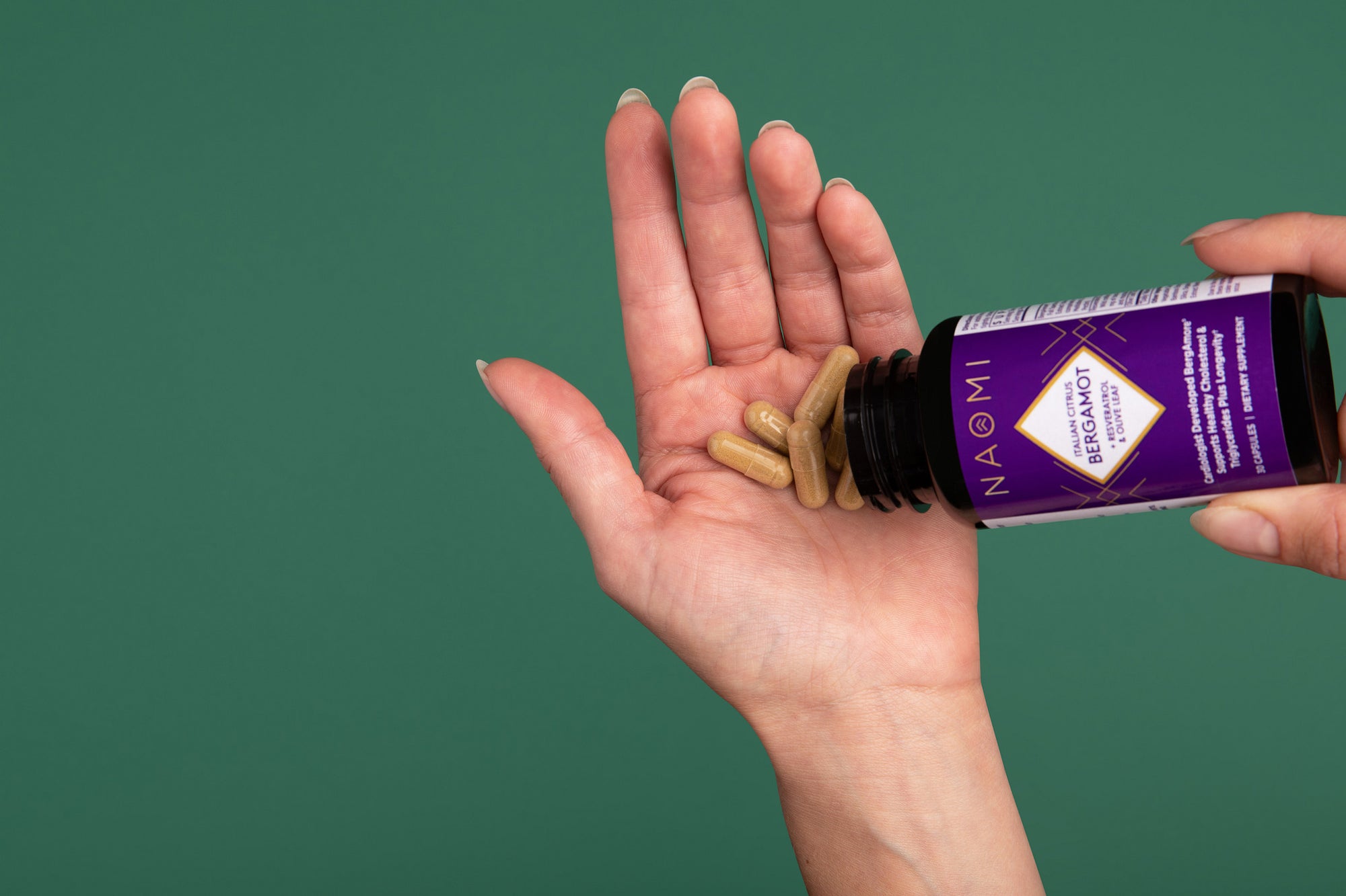 Hand pouring supplements from a bottle labeled 'NAOMI' onto a palm against a green background