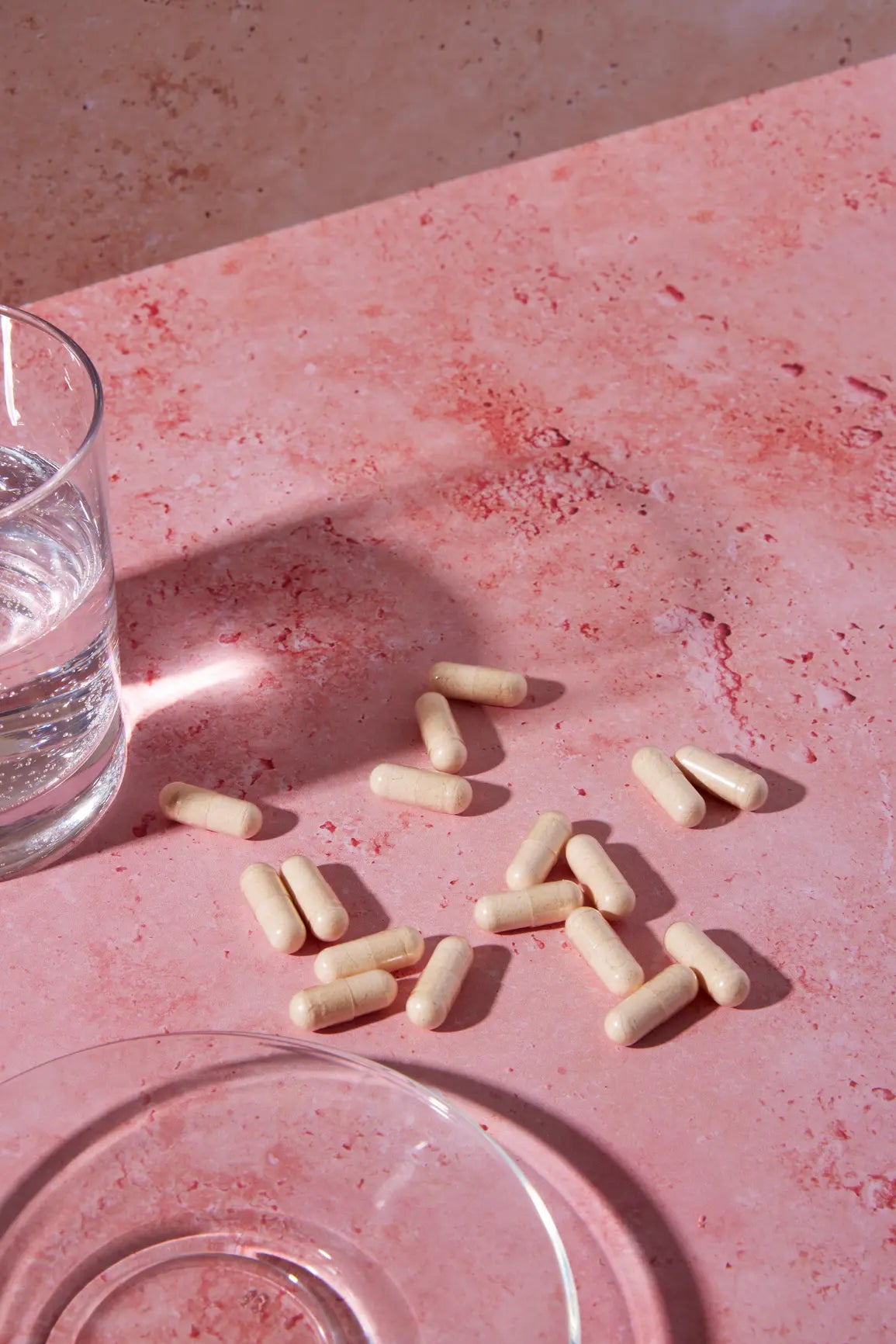 White capsules on a pink surface with a glass of water